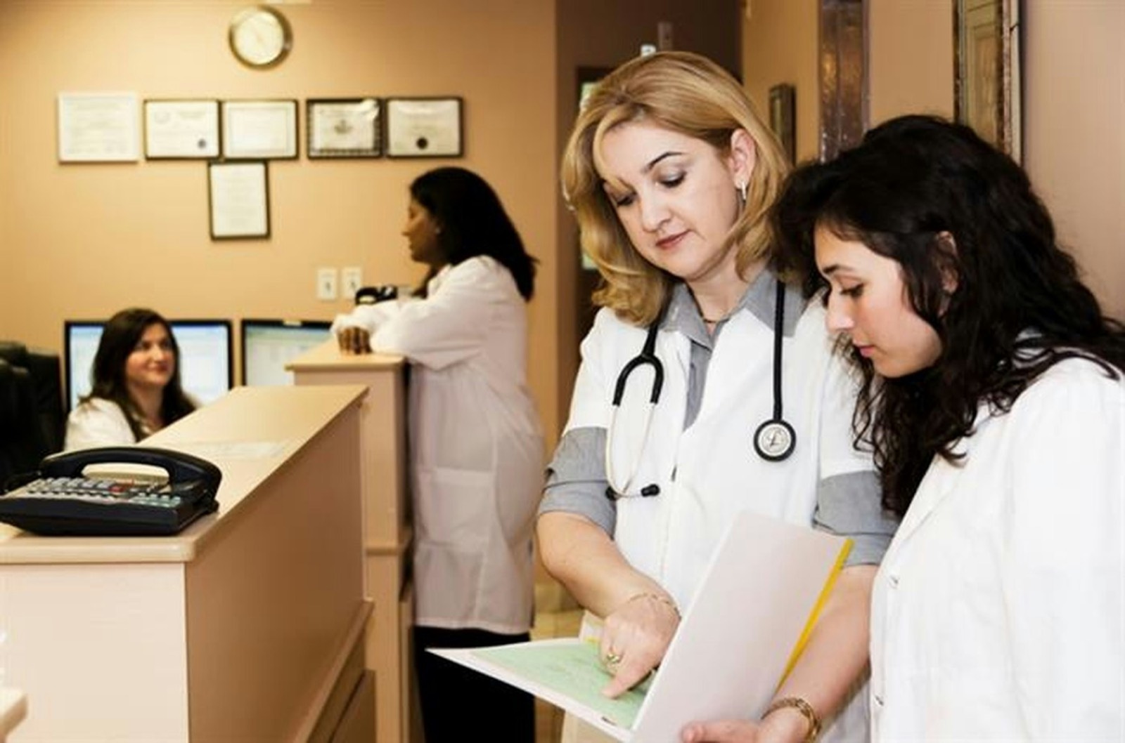 A woman at a clinic reception desk handing over a folder of papers