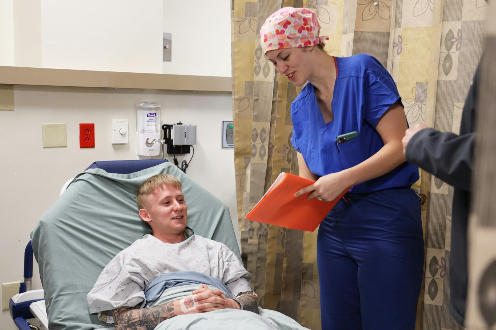 A nurse with a clipboard talking to a man resting in a hospital bed