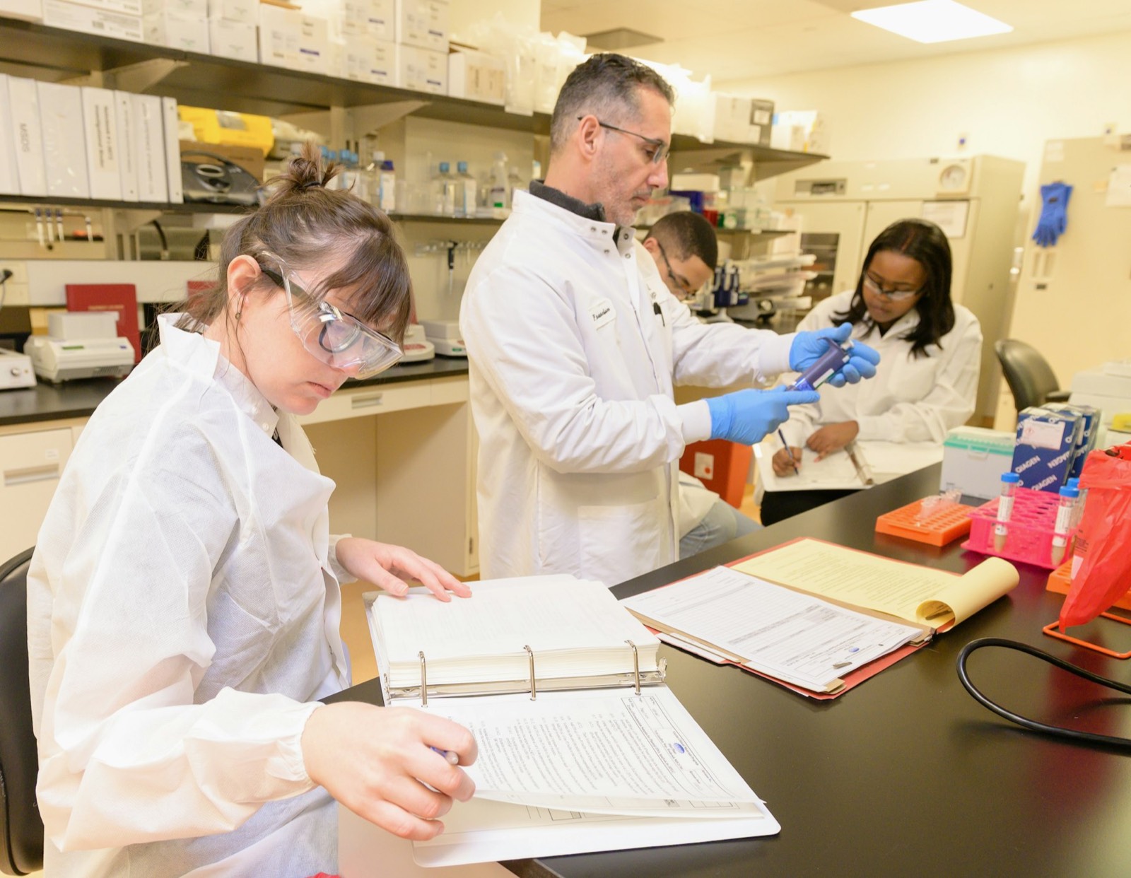 Researchers in white coats working at a laboratory bench with notebooks and samples
