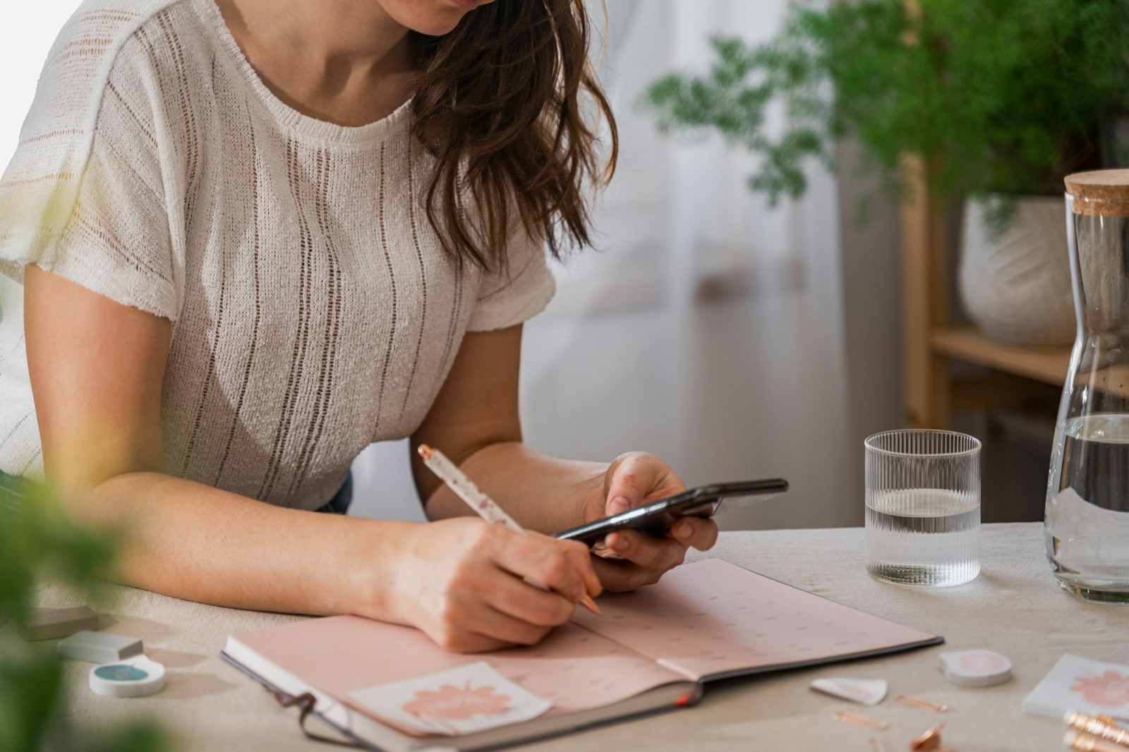 A woman at a table writing notes beside her phone
